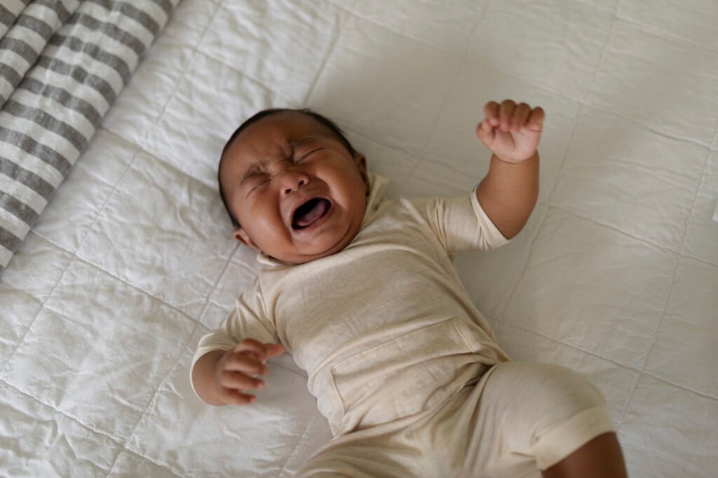 Crying baby lying on bed—highlighting wake-ups caused by feeding to sleep and the need to stop feeding to sleep for better rest.