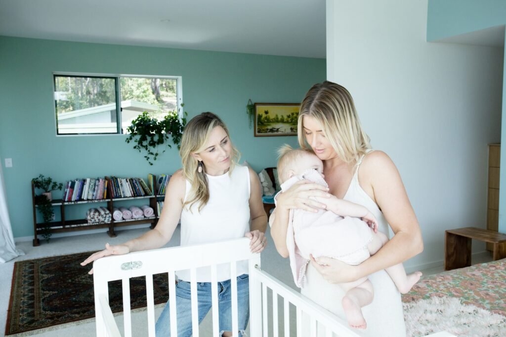 Elaine Harvey gently guiding a new mother through settling techniques beside her baby’s cot—offering real support beyond just a sleep schedule